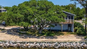 Une maison avec un grand arbre devant, une zone sablonneuse et une côte rocheuse.