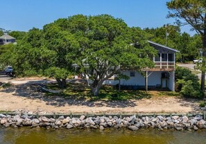 Una casa con un grande albero di fronte, una spiaggia sabbiosa e un litorale roccioso.