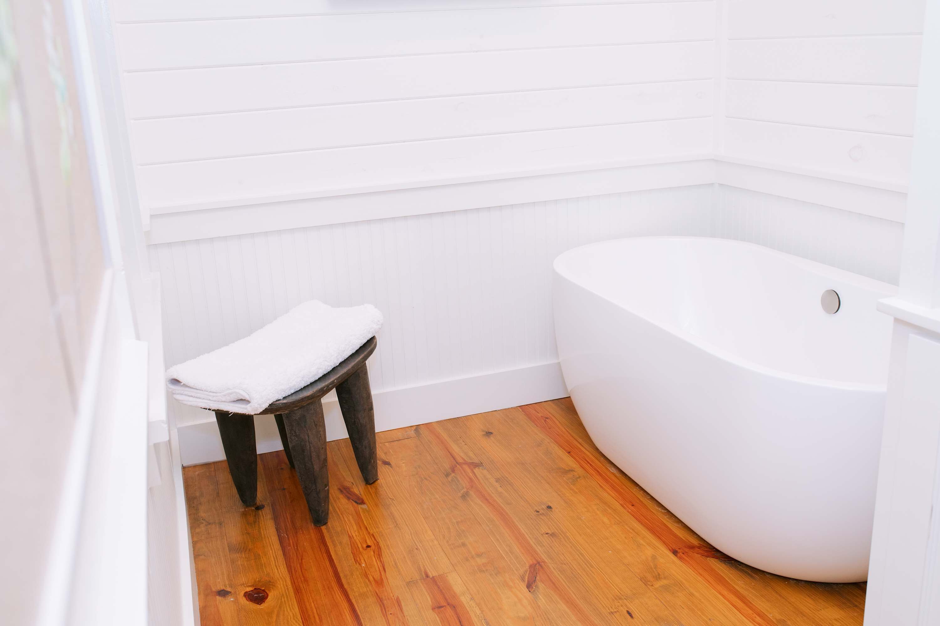 Un baño con suelo de madera, una bañera blanca y un taburete pequeño con una toalla.