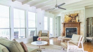 Un salon spacieux doté d’une cheminée, de grandes fenêtres et d’un ventilateur de plafond.
