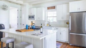 Une cuisine moderne avec des meubles blancs, un réfrigérateur en acier inoxydable et un îlot central doté de tabourets.