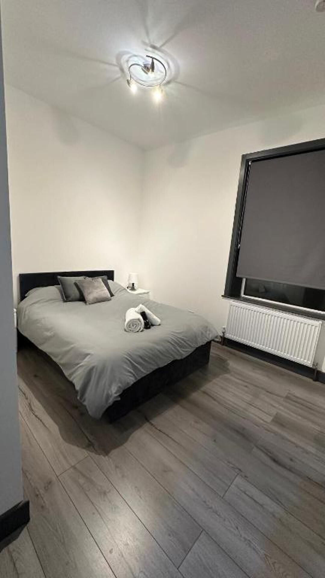 A bedroom with a bed, a nightstand, a window, and a radiator.