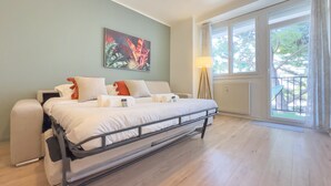 A bedroom with a bed, a standing lamp, a window with a view of trees, and a painting on the wall. - Le Palm (Cannes)