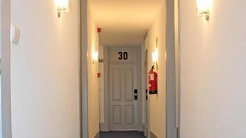 Un pasillo estrecho con alfombra azul, paredes blancas y una puerta con el número 30.