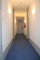 Un pasillo estrecho con alfombra azul, paredes blancas y una puerta con el número 30.