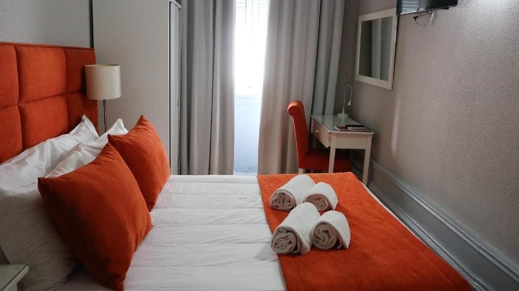 A hotel room with a bed, pillows, a desk, and a chair.