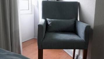 A room with a dark grey armchair, a wooden floor, and a window with curtains.