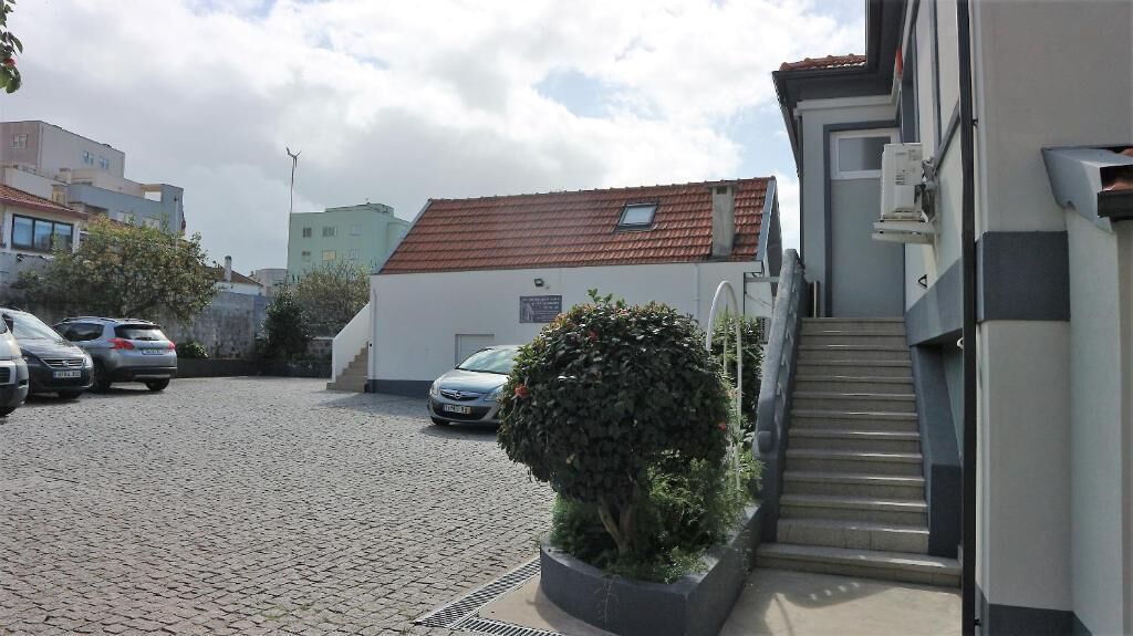 Uma área de estacionamento com carros, uma escadaria que leva a um edifício e um pequeno arbusto.