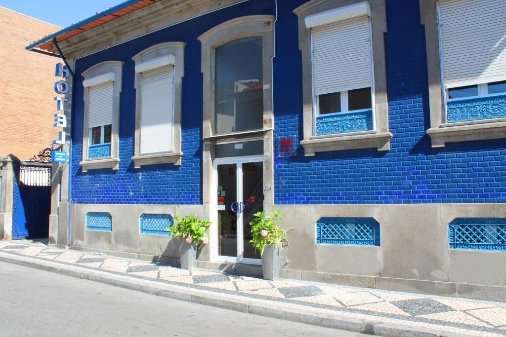 Hotel com fachada azul, janelas amplas e entrada visível.