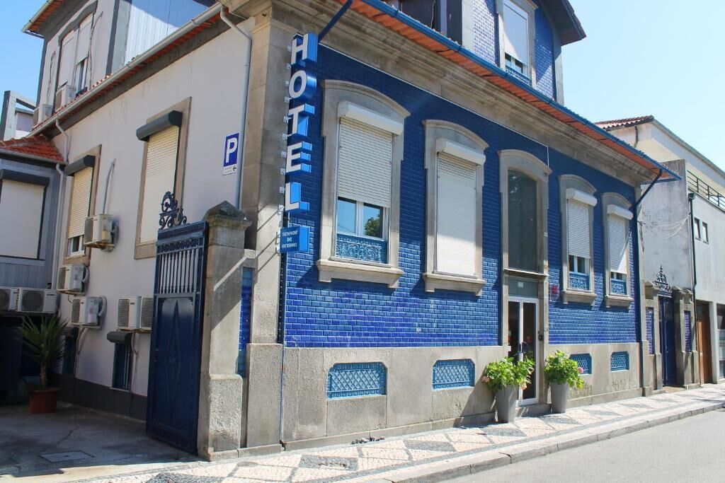 Hotel com fachada azul, entrada fechada por portão e placa de estacionamento.