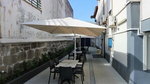 Un patio al aire libre con mesas y sillas, un paraguas grande y un muro de piedra.