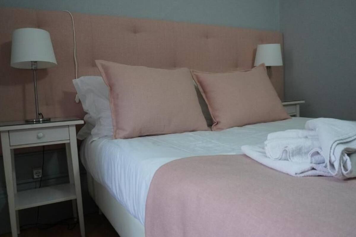 Un lit bien fait, avec une tête de lit rose, une literie blanche et deux lampes de chevet.