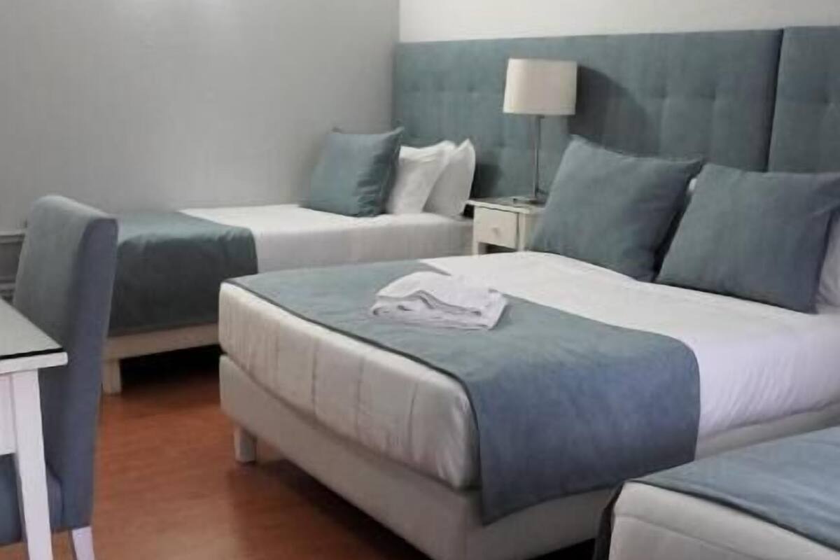 Une chambre d’hôtel avec deux lits simples, un lit double, un bureau et une chaise.