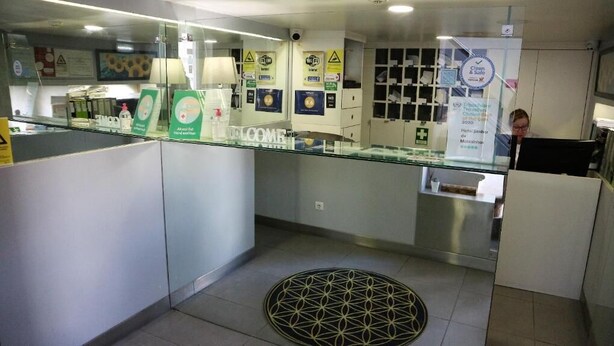 Een receptiezone met een glazen scheidingswand, informatieposters en een betegelde vloer.