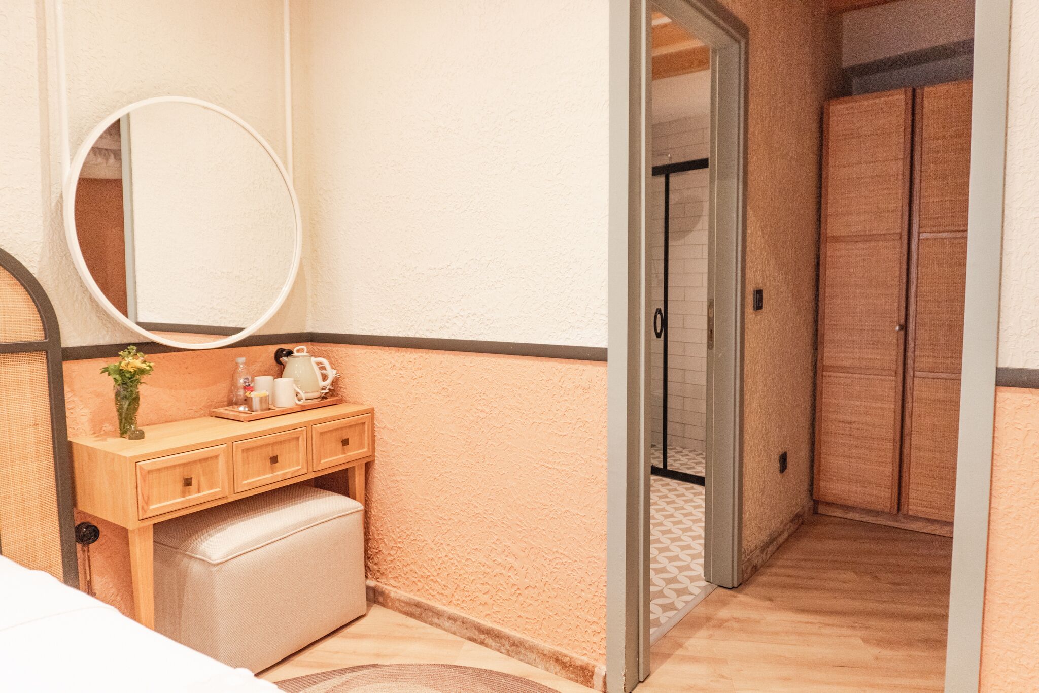 Un dormitorio con un aparador de madera, un espejo redondo y una mesita de noche con un jarrón y una tetera.