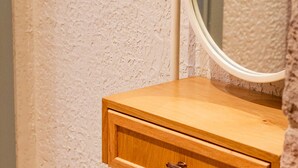 A bathroom with a wooden vanity, a round stool, and a textured wall. - Qara Otel (Ayvalik)