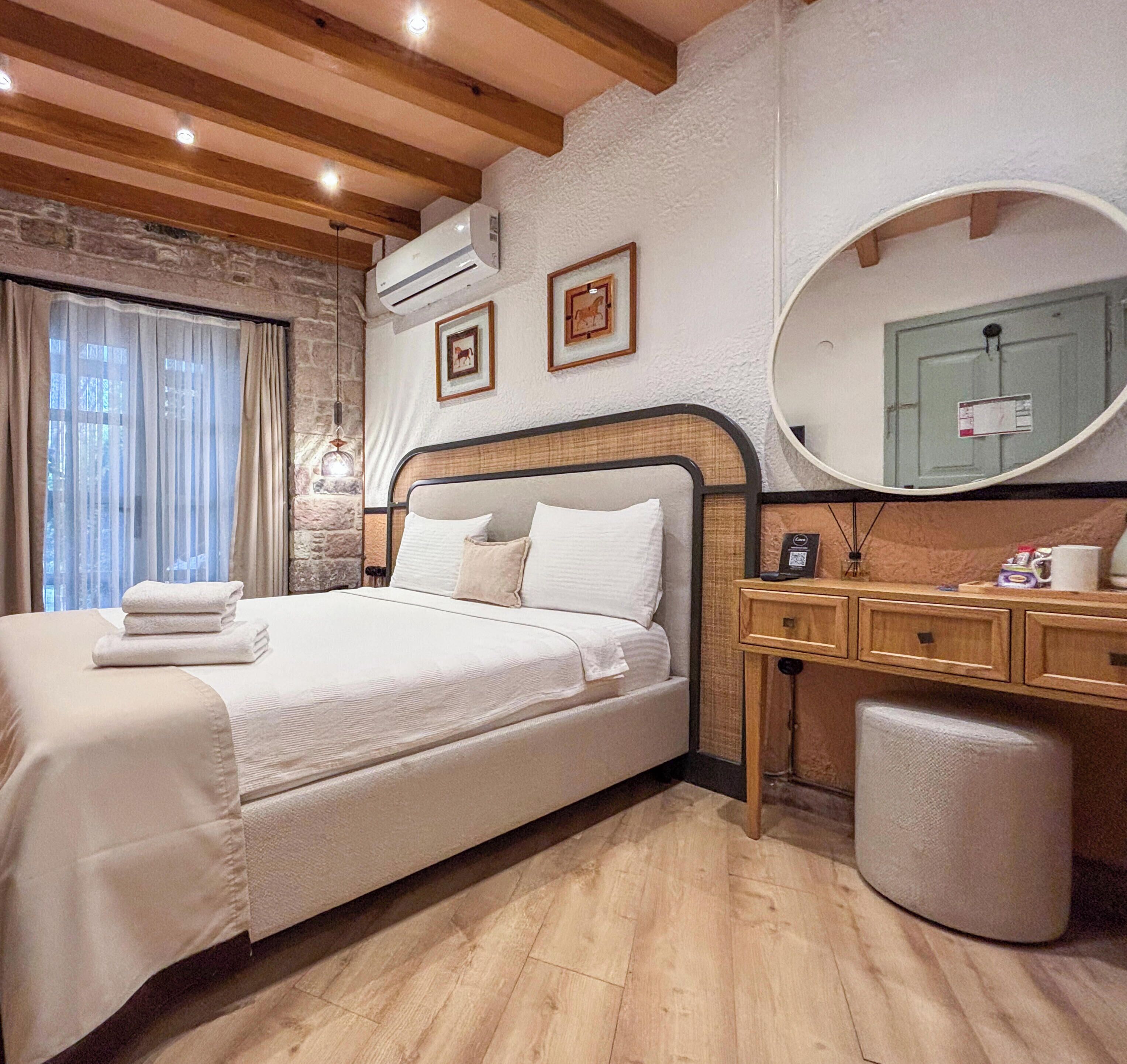 A hotel room with a bed, bedside table, mirror, and a stone wall.