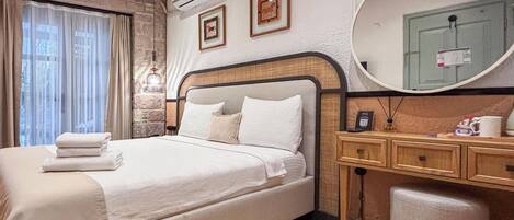 A hotel room with a bed, bedside table, mirror, and a stone wall.