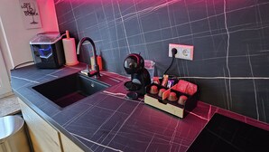 Une cuisine moderne dotée d’un plan de travail en marbre noir, d’une machine à café et d’une bouilloire rouge.