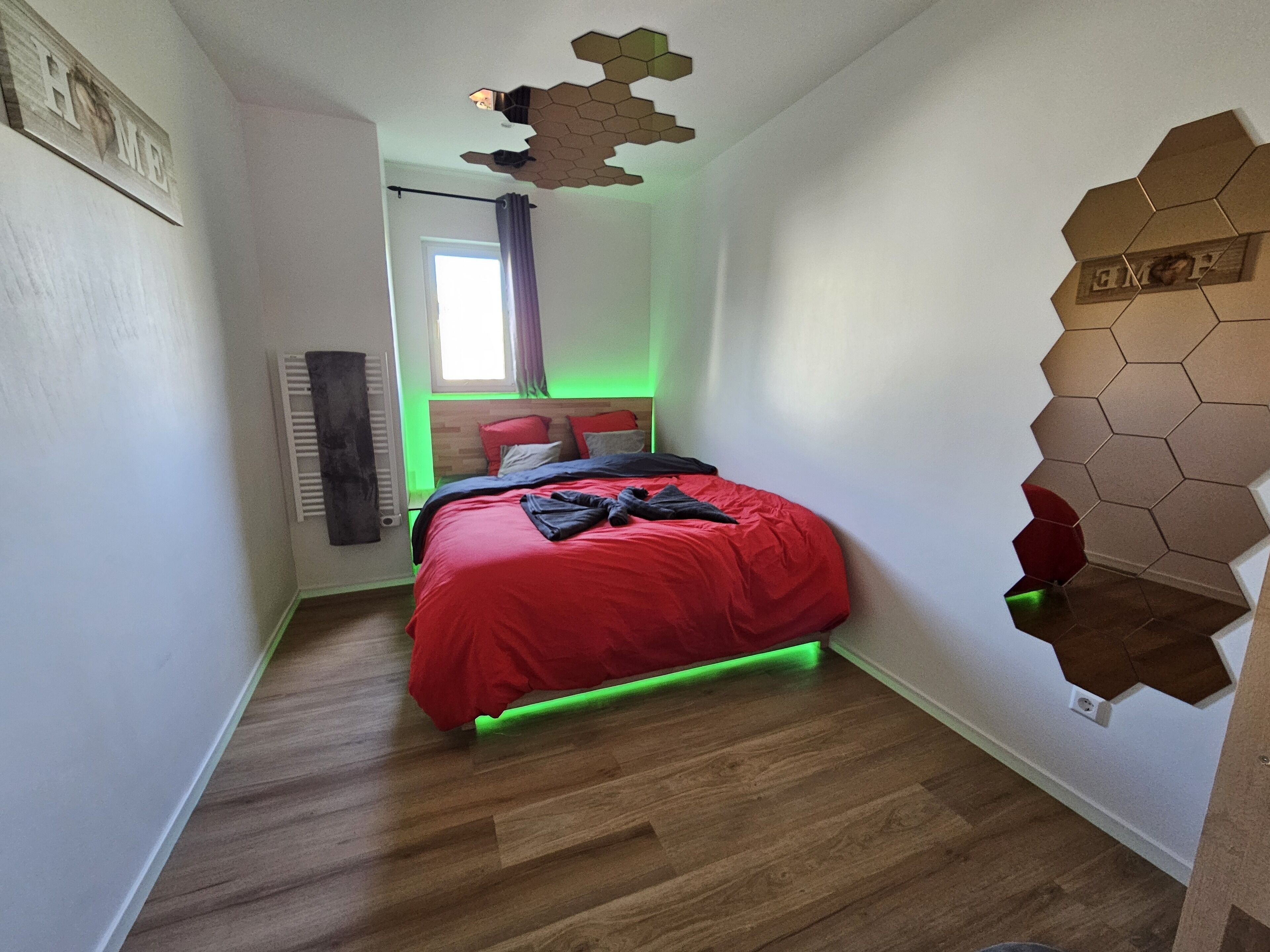A bedroom with a wooden floor, a red bed, and a unique hexagonal wall design.