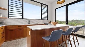 A modern kitchen with a large island, wooden cabinets, and a view of the outdoors.