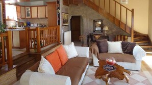 A spacious living area with a staircase, wooden furniture, and a kitchen in the background. - Traditional Villa Gardenia in Skiathos (Skiathos)