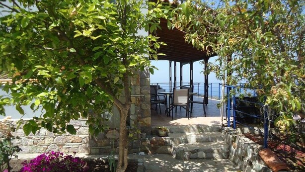 A covered outdoor seating area with stone steps leading to a table and chairs, overlooking a body of water. - Traditional Villa Gardenia in Skiathos (Skiathos)