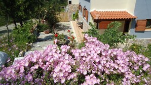 A house with a tiled roof, a stone pathway, and a garden with pink flowers. - Traditional Villa Gardenia in Skiathos (Skiathos)