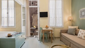 Una habitación acogedora con un sofá, una mesa de comedor con sillas, un televisor en la pared y una maleta en el suelo.
