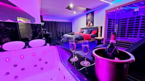 A modern bedroom with a bed, a jacuzzi tub, and a champagne bottle. - Magnifique Suite Spa Luxembourg (Differdange)