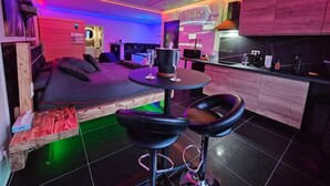 A modern, compact living space with a sofa, a small dining table, and two bar stools. - Magnifique Suite Spa Luxembourg (Differdange)