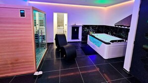 A modern bathroom with a jacuzzi, a glass shower enclosure, and a black chair. - Magnifique Suite Spa Luxembourg (Differdange)