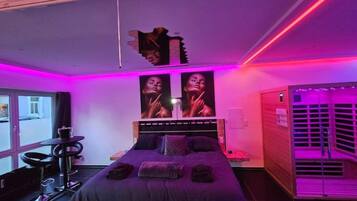 Ein modernes Schlafzimmer mit Bett, einer Bank, einem Schreibtisch und einem Fenster.