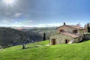 A stone house with a sloped roof, situated on a grassy hillside with a view of rolling hills in the background. - A Great Villa and a Cozy Cottage sleeps 10 with 6 bathroom and 2 pools! Amazing! (Baschi)