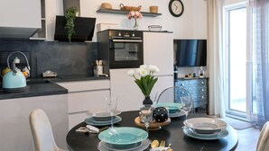 Cocina moderna con comedor, que presenta una encimera negra, armarios blancos y una mesa de comedor con platos azules y flores blancas.