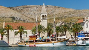 Un pueblo costero con una destacada torre de iglesia, un muelle con barcos y palmeras.