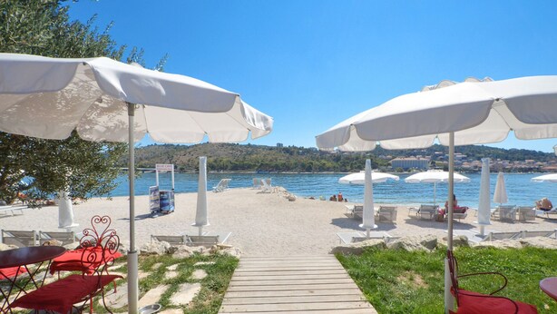 Zona de playa con sombrillas blancas, sillas rojas y un sendero de madera que conduce a la playa.