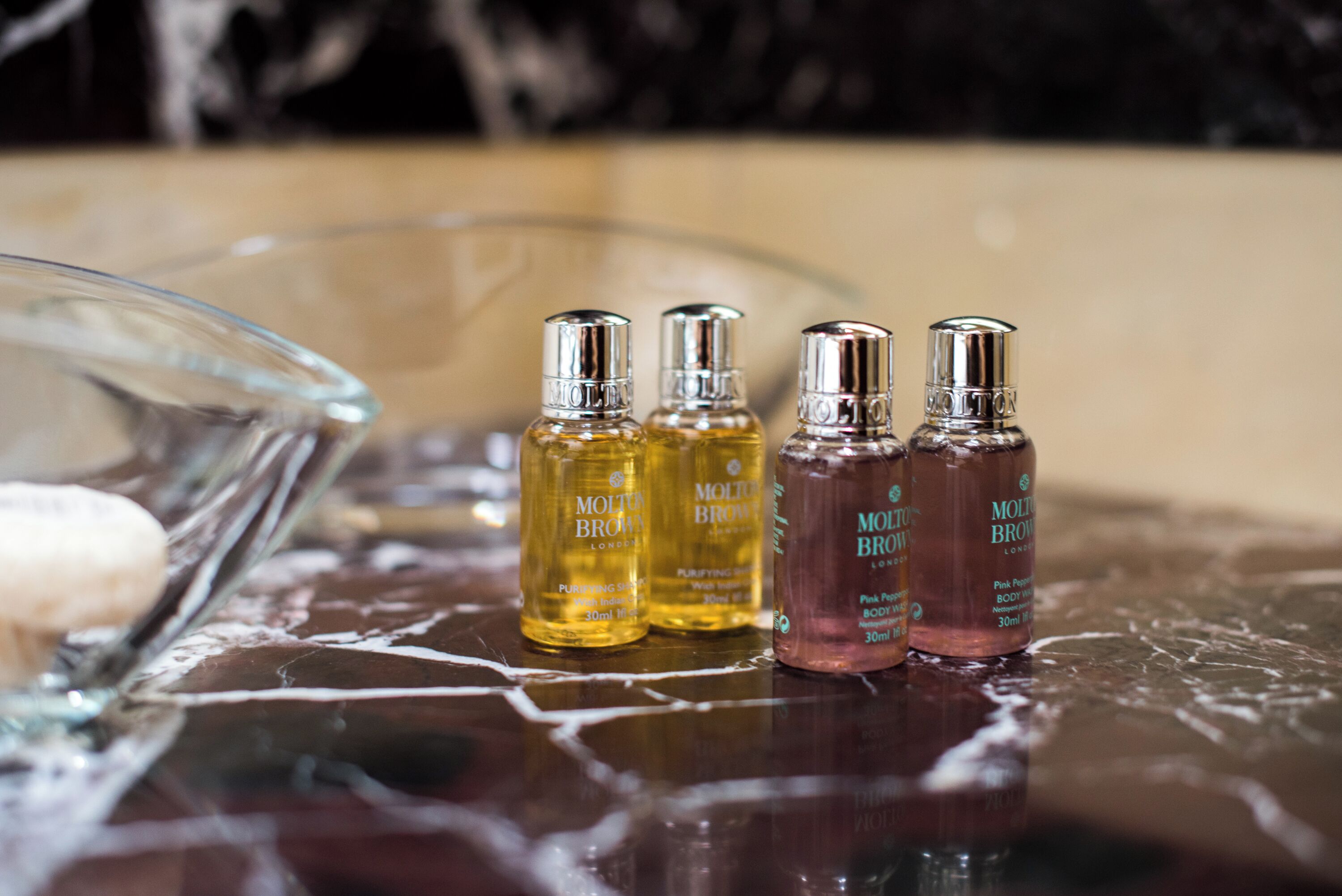 Four bottles of Molton Brown body lotion on a reflective surface.