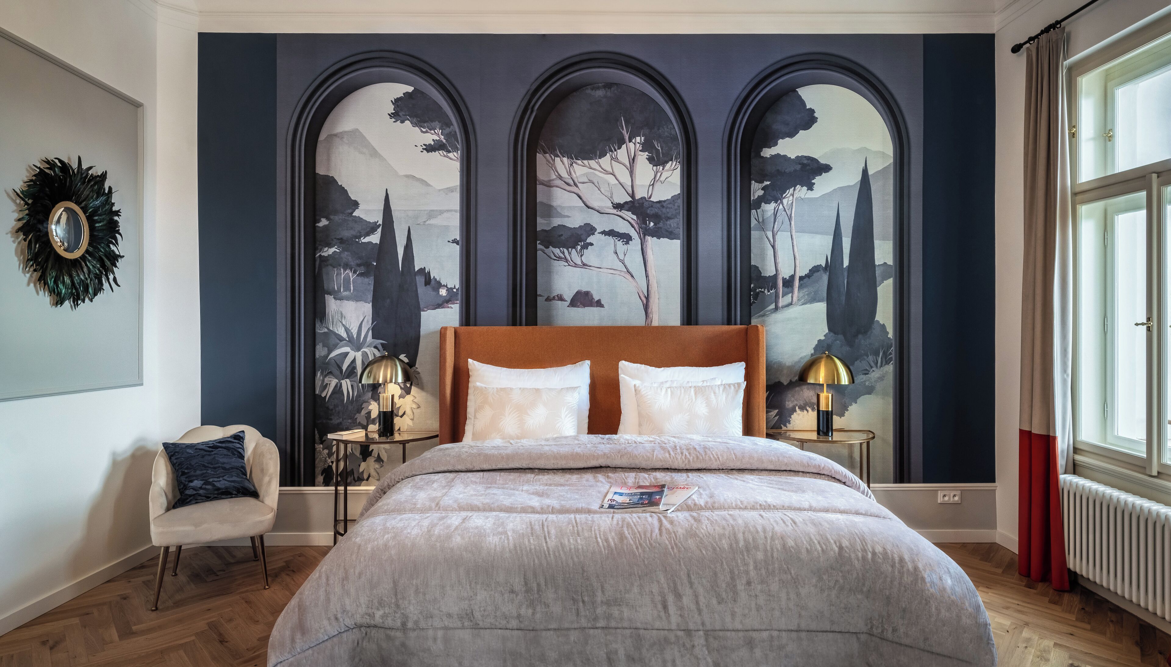 Une chambre à coucher avec un grand lit, une table de chevet, une chaise et trois panneaux muraux en forme d’arc ornés de peintures de paysages.