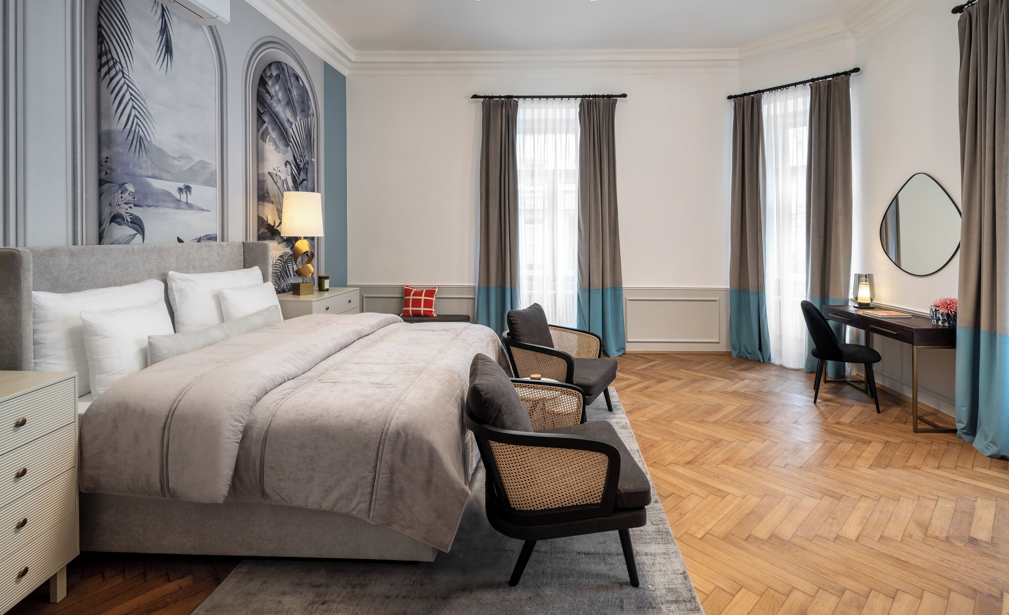 Una habitación de hotel moderna con una cama grande, un escritorio, dos sillas y un amplio ventanal con cortinas.