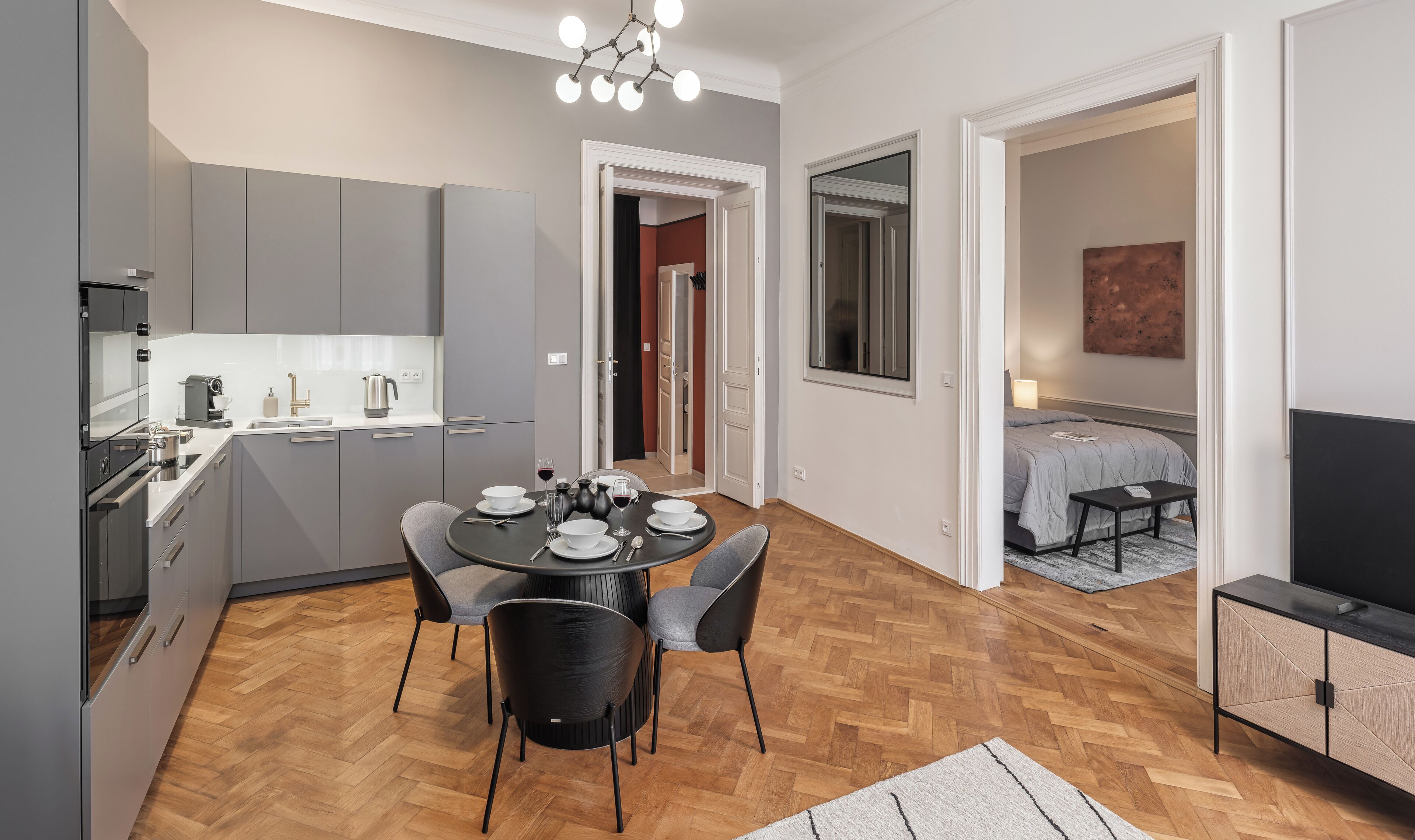Una cocina moderna con armarios grises, una mesa de comedor para cuatro personas y un área de comedor independiente con una cama y un televisor.