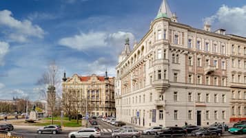 A historic building with classical architecture, a street with parked cars, and a clear sky.