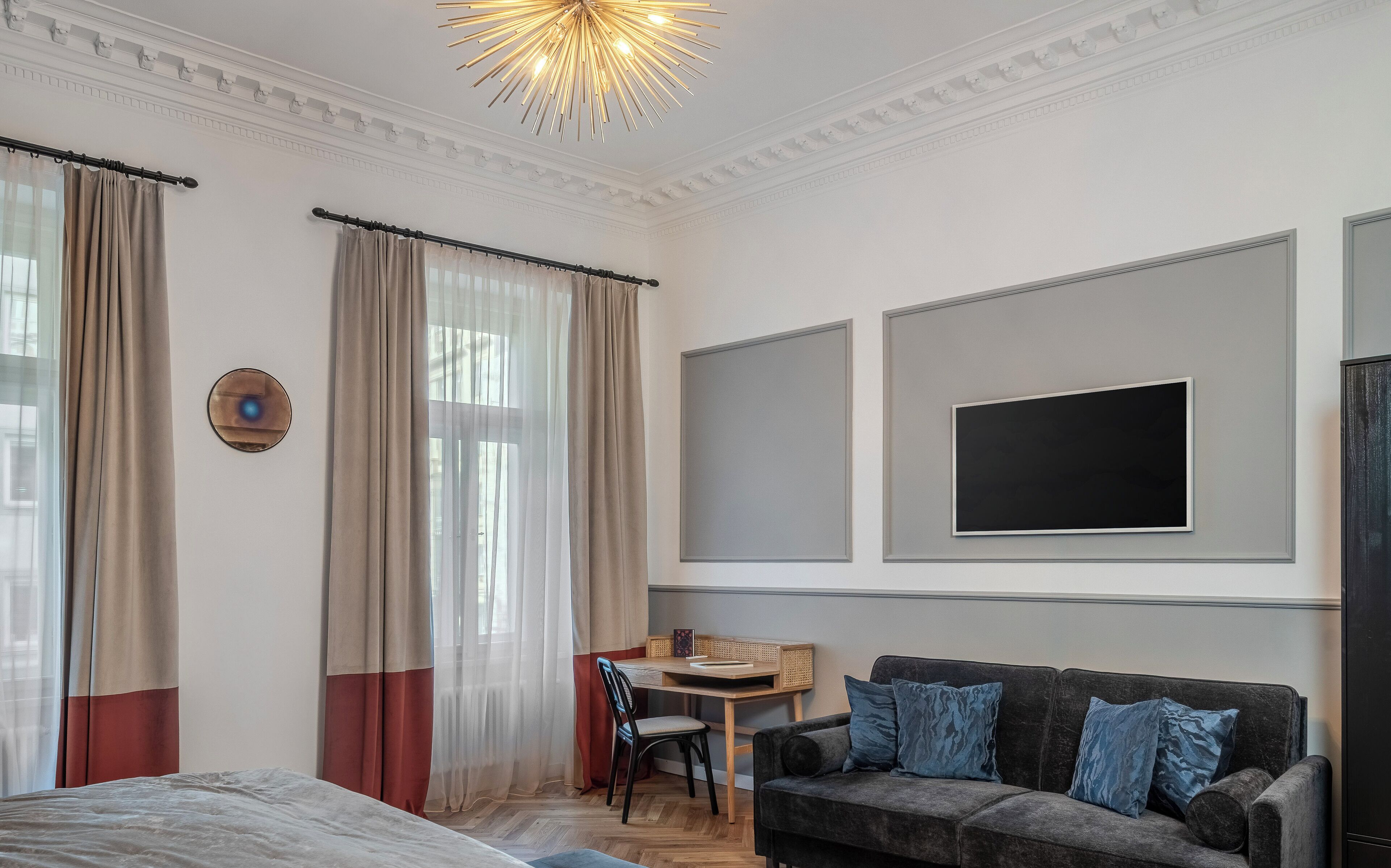 A hotel room with a bed, a desk with a chair, a sofa, and a TV mounted on the wall.