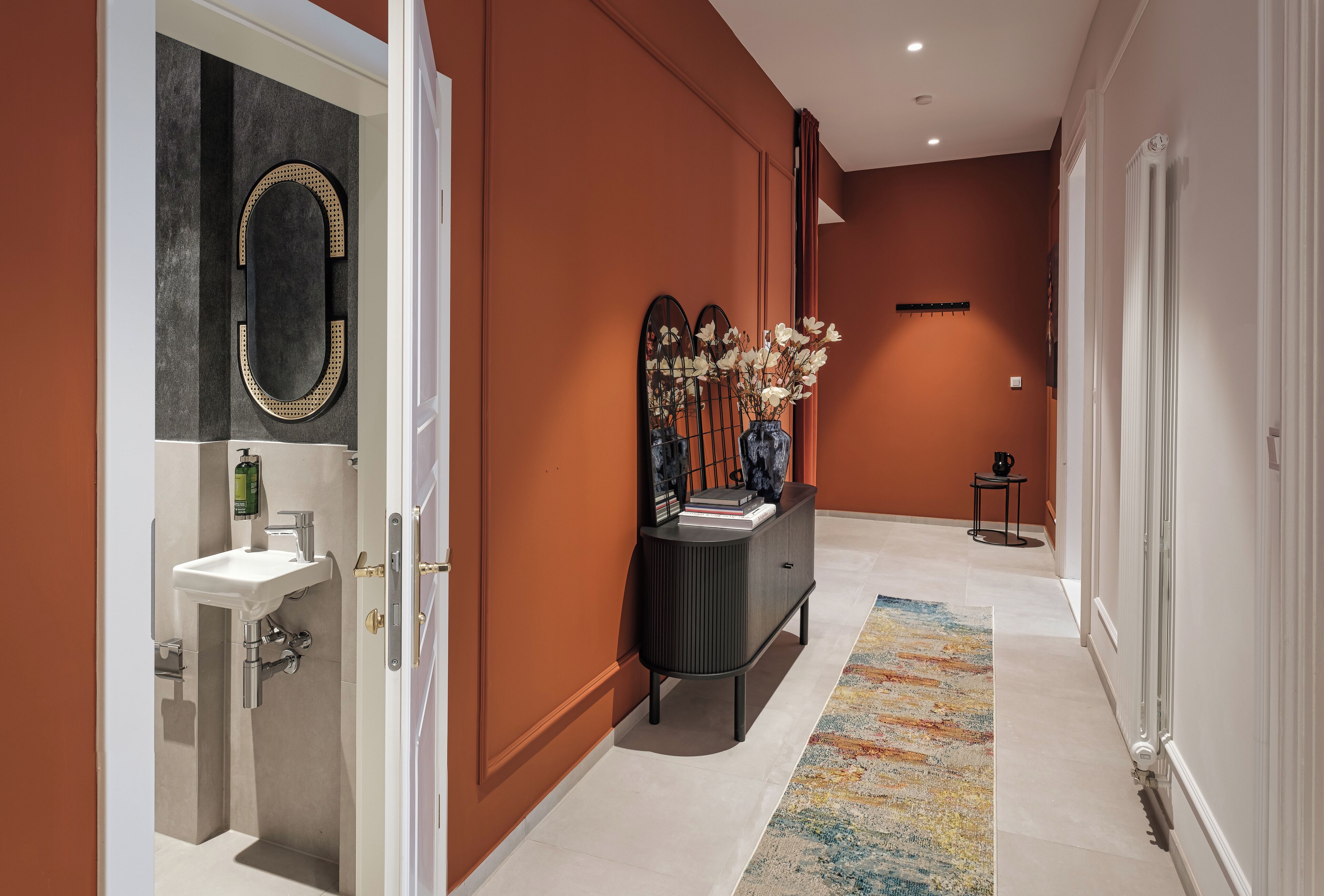A hallway with a white sink, a mirror, a console table with decorative items, and a patterned rug.