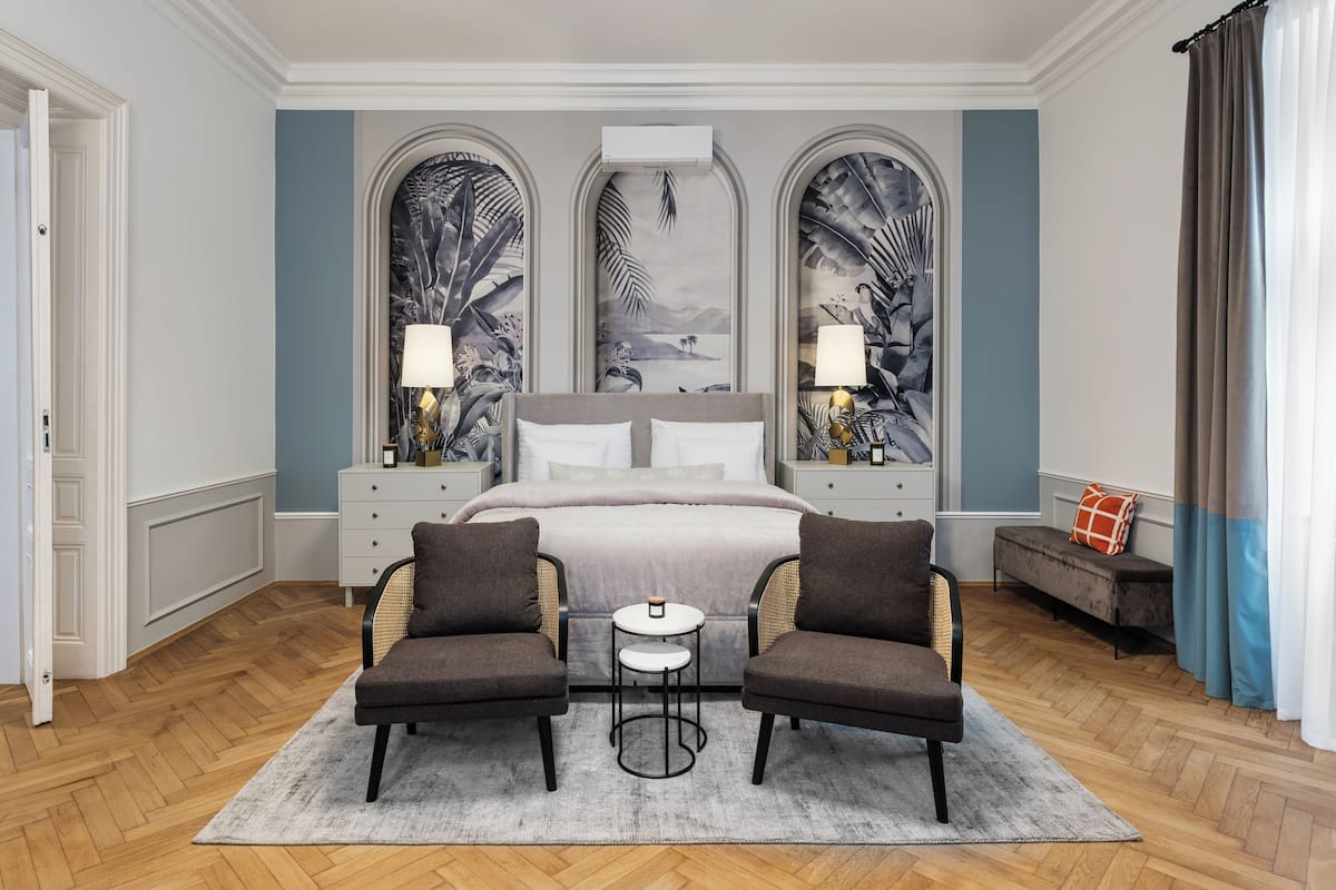 A bedroom with a large bed, two armchairs, a small table, and a bench.