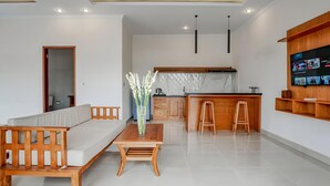 Ein modernes Wohnzimmer mit Sofa, Couchtisch aus Holz und Küchenbereich mit Marmorfliesenspiegel und Holzschränken.