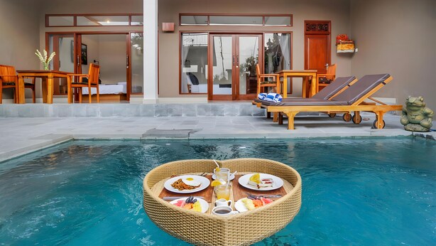 Ein Essbereich am Pool mit einem schwimmenden Tisch, Liegestühlen und einer dekorativen Froschstatue.