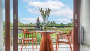 Ein Balkon mit einem Holztisch und zwei Stühlen, einer Pflanzvase mit Grünpflanzen und Blick auf einen Tempel und Vegetation.