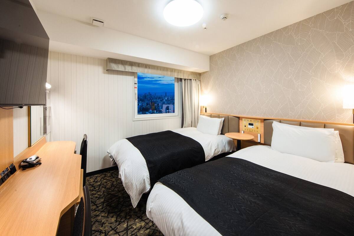 Hotelkamer met twee bedden, een bureau, een telefoon en een raam met uitzicht op de stad.