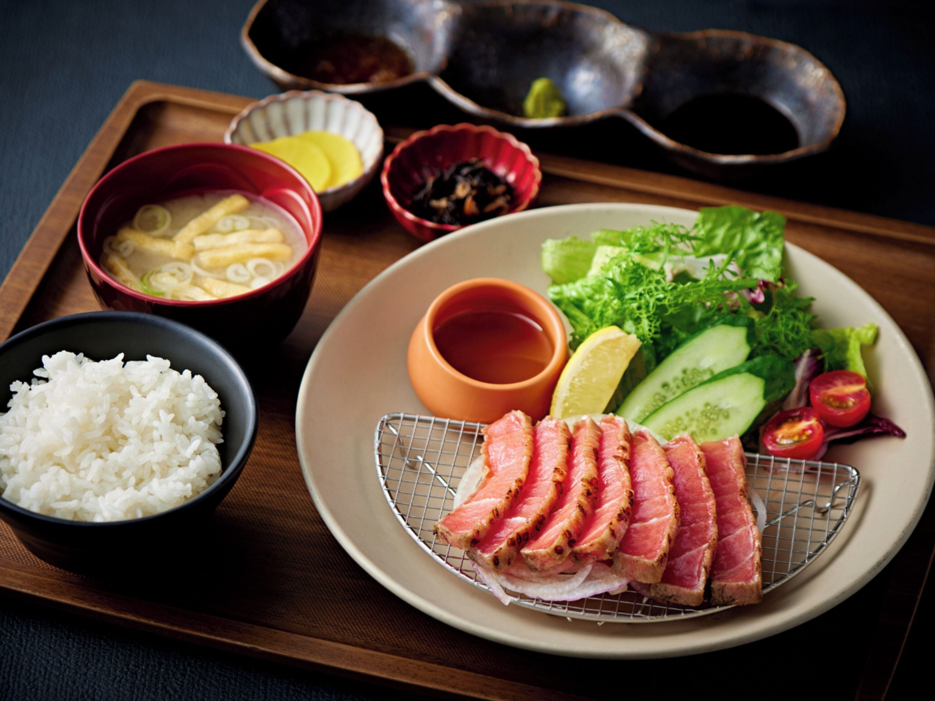 A tray with a plate of sliced meat, a bowl of rice, and various side dishes.